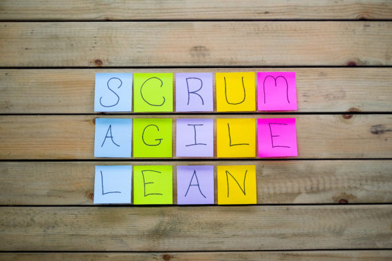A wooden board with sticky notes spelling out the words scrum agile & lean. The post-it notes spell out the management technique used with scurm agile and lean start-up.